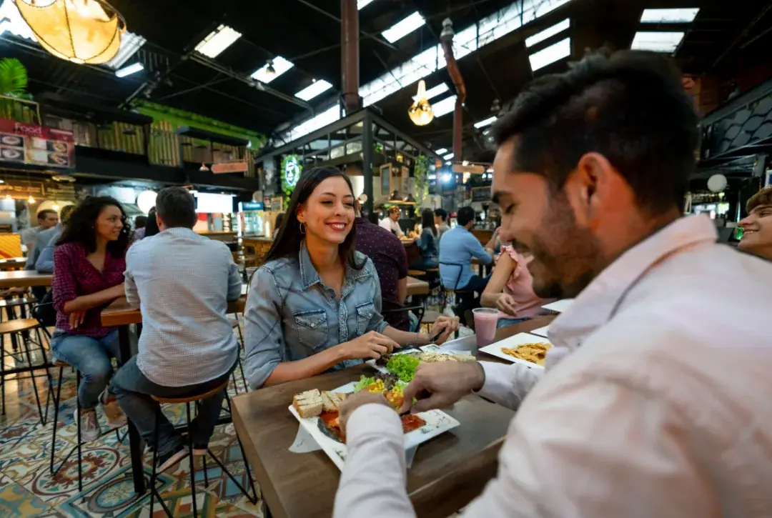 Friends laughing over a meal at a bustling food hall